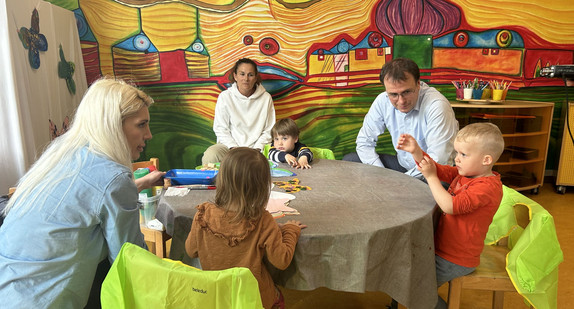 Staatssekretär Volker Schebesta sitzt mit Kindern und Auszubildenden des Direkteinstiegs Kita an einem Tisch.